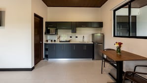 Une cuisine moderne avec des meubles de couleur sombre, un réfrigérateur en acier inoxydable et un coin repas comprenant une table et des chaises en bois.