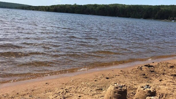 Hiekkainen ranta, jossa on tyyni järvi ja metsäinen rantaviiva.