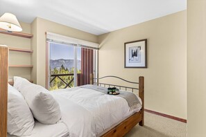 A bedroom with a bed, a nightstand, a lamp, a window with a view of mountains, and a framed picture on the wall. - Whispering Pines 3BR Townhouse Views + Hot Tub (Golden)