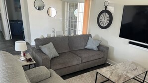 A living room with a grey sofa, a coffee table, a TV, and a clock on the wall. - Perfect 3-bedroom house with AC in Fort Myers Beach (Fort Myers Beach)