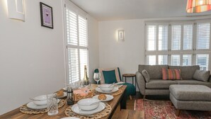 A dining area with a wooden table set for a meal, a grey sofa, and a patterned rug. - Betty's Buoy (Weymouth)