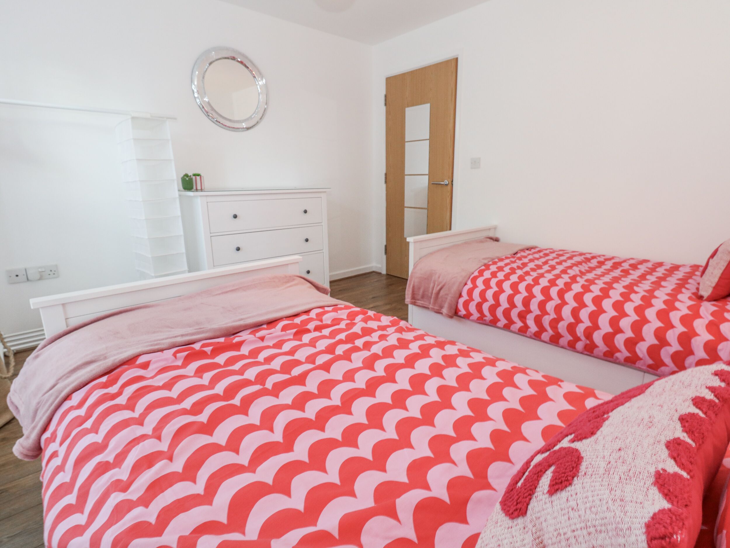 A bedroom with two beds, a white dresser, a mirror, and a wooden door.
