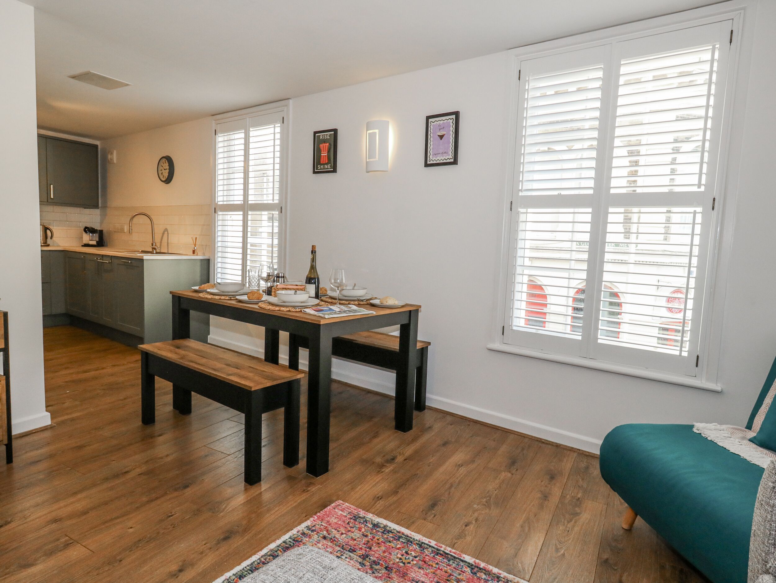 A modern kitchen with a dining area, wooden flooring, and a view through large windows.