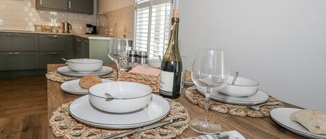 A dining table set with white plates, bowls, and cutlery, a bottle of wine, and a menu.