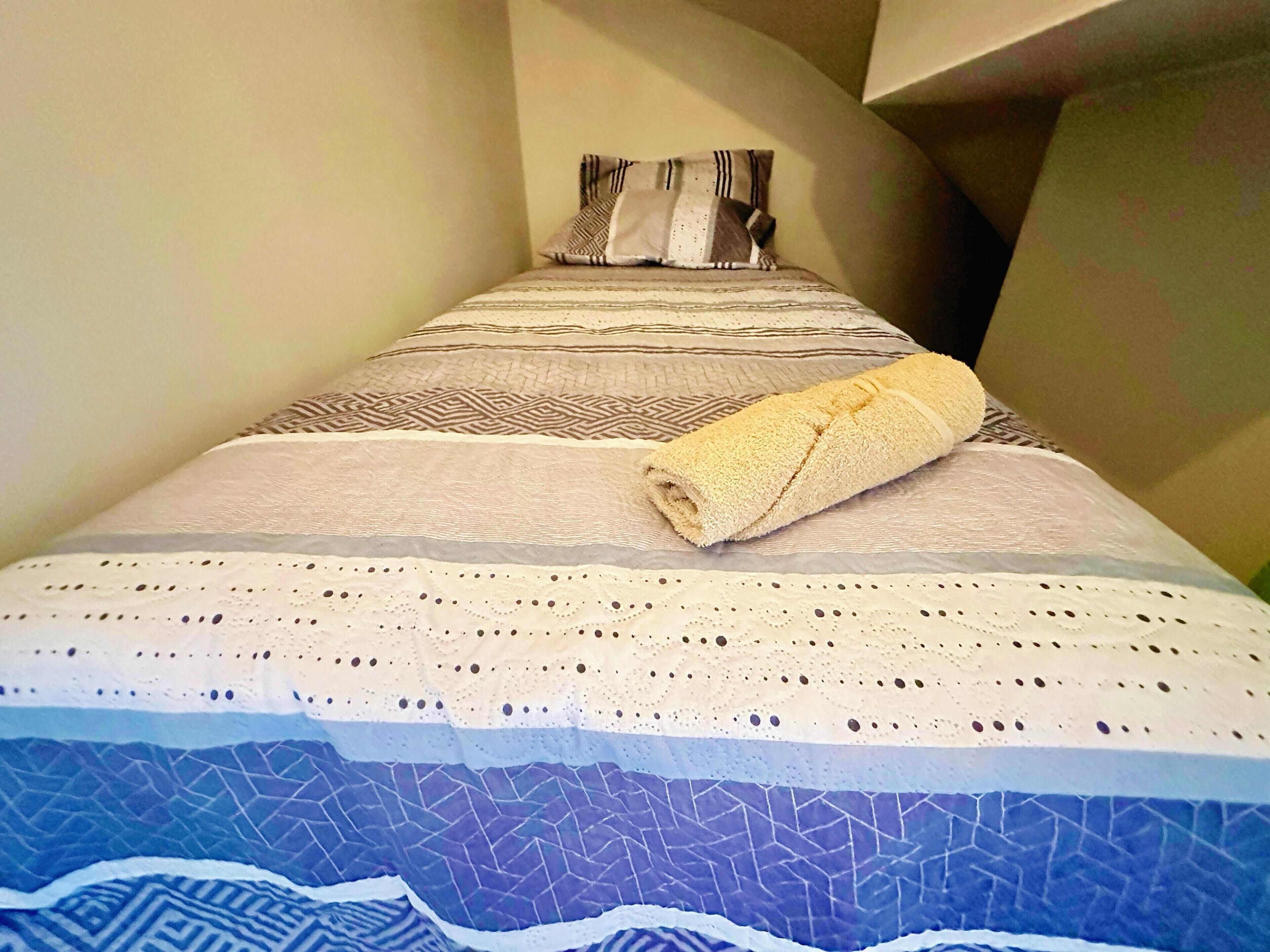Ein ordentlich gemachtes Bett mit gemusterten Betttextilien und einem aufgerollten Handtuch darauf.
