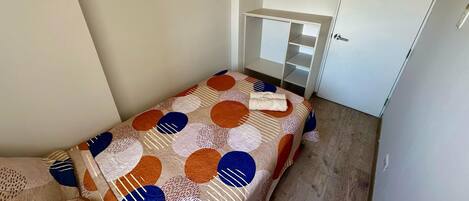 Una habitación pequeña y funcional con cama, armario blanco y escritorio integrado.