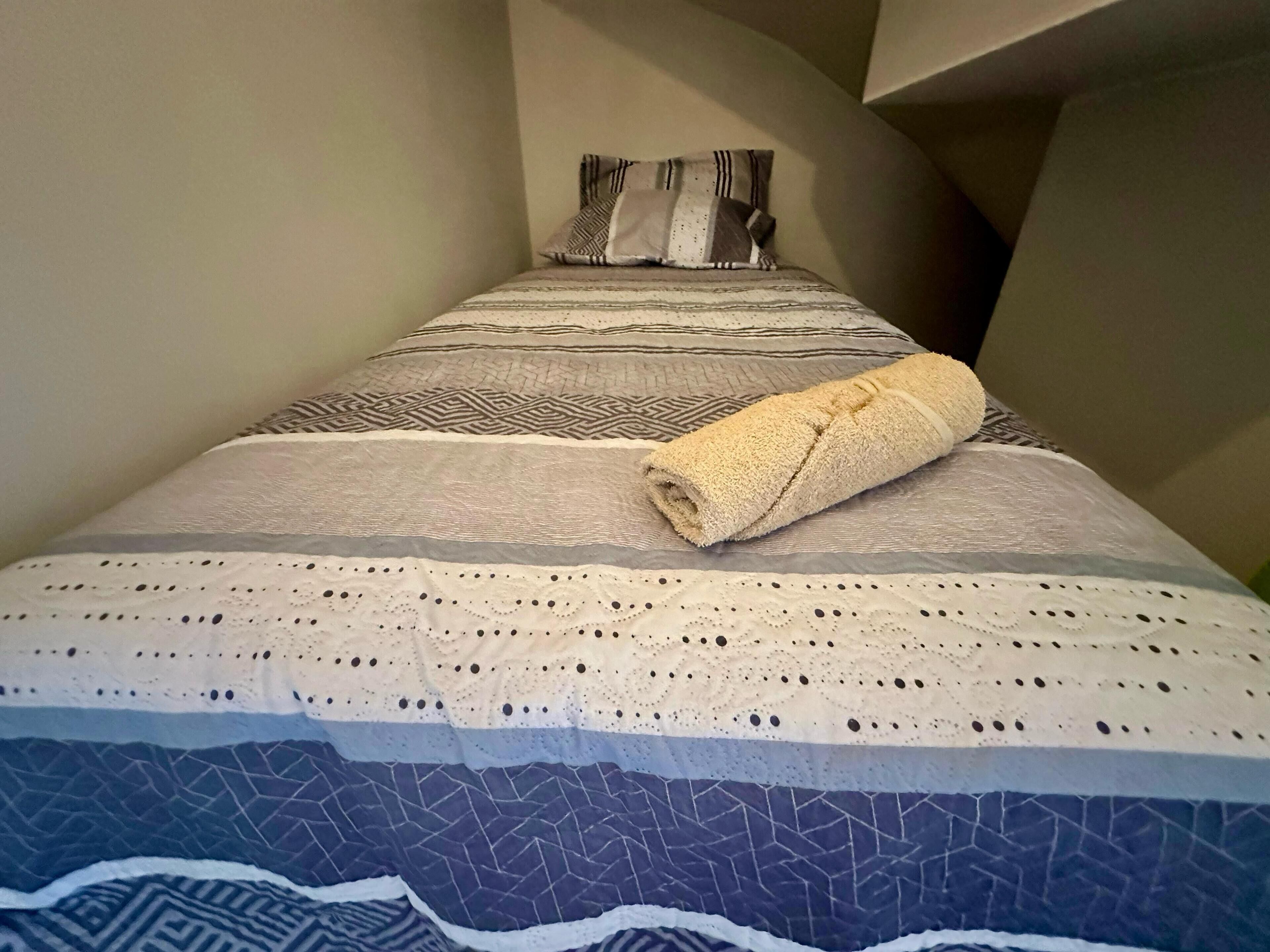 Ein ordentlich gemachtes Bett mit gemusterten Betttextilien und einem aufgerollten Handtuch darauf.