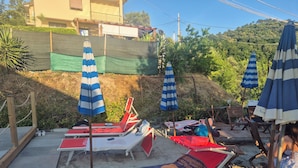 Eine Strandbucht mit Liegestühlen, gestreiften Sonnenschirmen und einer Holzterrasse.
