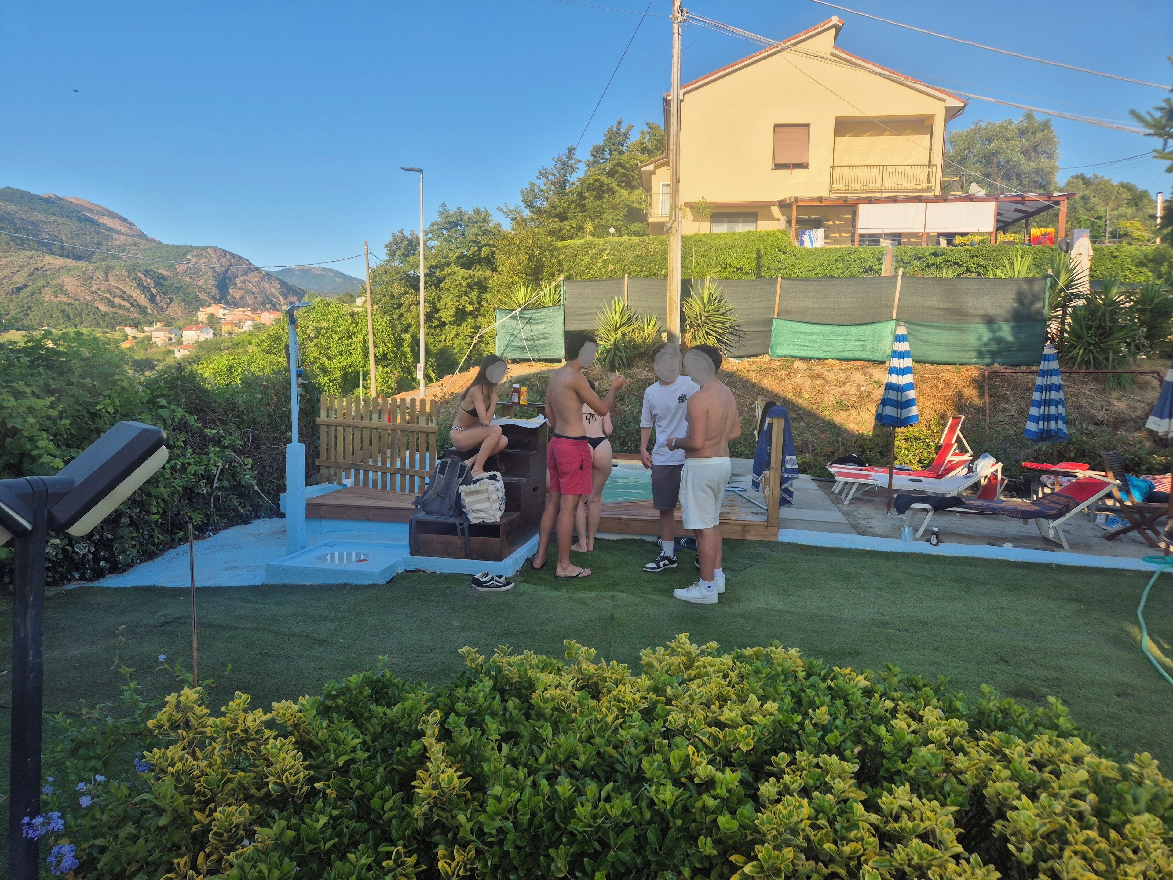 Zona de piscina con muelle de madera, sillas de descanso y sombrillas.