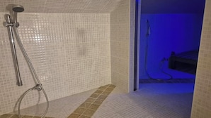 Ein Badezimmer mit Dusche, gefliesten Wänden und Abfluss.