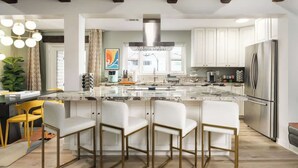 Een moderne keuken met witte kastjes, een groot eiland met barstoelen, een roestvrijstalen koelkast en een hanglamp.