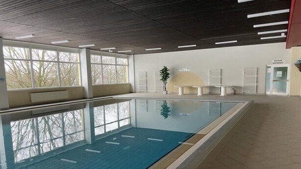 Ein hallenbad mit großen Fenstern, gefliestem Boden und einer Sitzbank an der Wand.