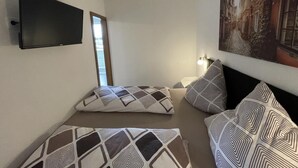 Ein Zimmer mit Bett, gemusterten Kissen, einem montierten Fernseher und einem Stadtbild.