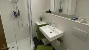 Ein modernes Badezimmer mit einer Duschkabine, einem weißen Waschbecken, einem Spiegel und einer Toilette.