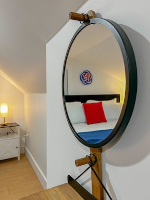 Una habitació amb un llit, una làmpada de nit i un mirall sobre un suport de fusta.
