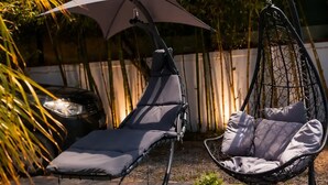 Dos sillones de exterior, una silla colgante y una mesa redonda con una vela y una planta.