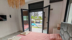 Un dormitorio moderno con una cama grande, televisión y vistas a una zona de piscina exterior.