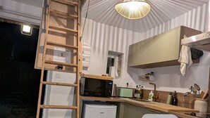 Eine kleine Küche mit einer Holzleiter, einer Mikrowelle, einem kleinen Kühlschrank und einem Essbereich mit einem Stuhl.