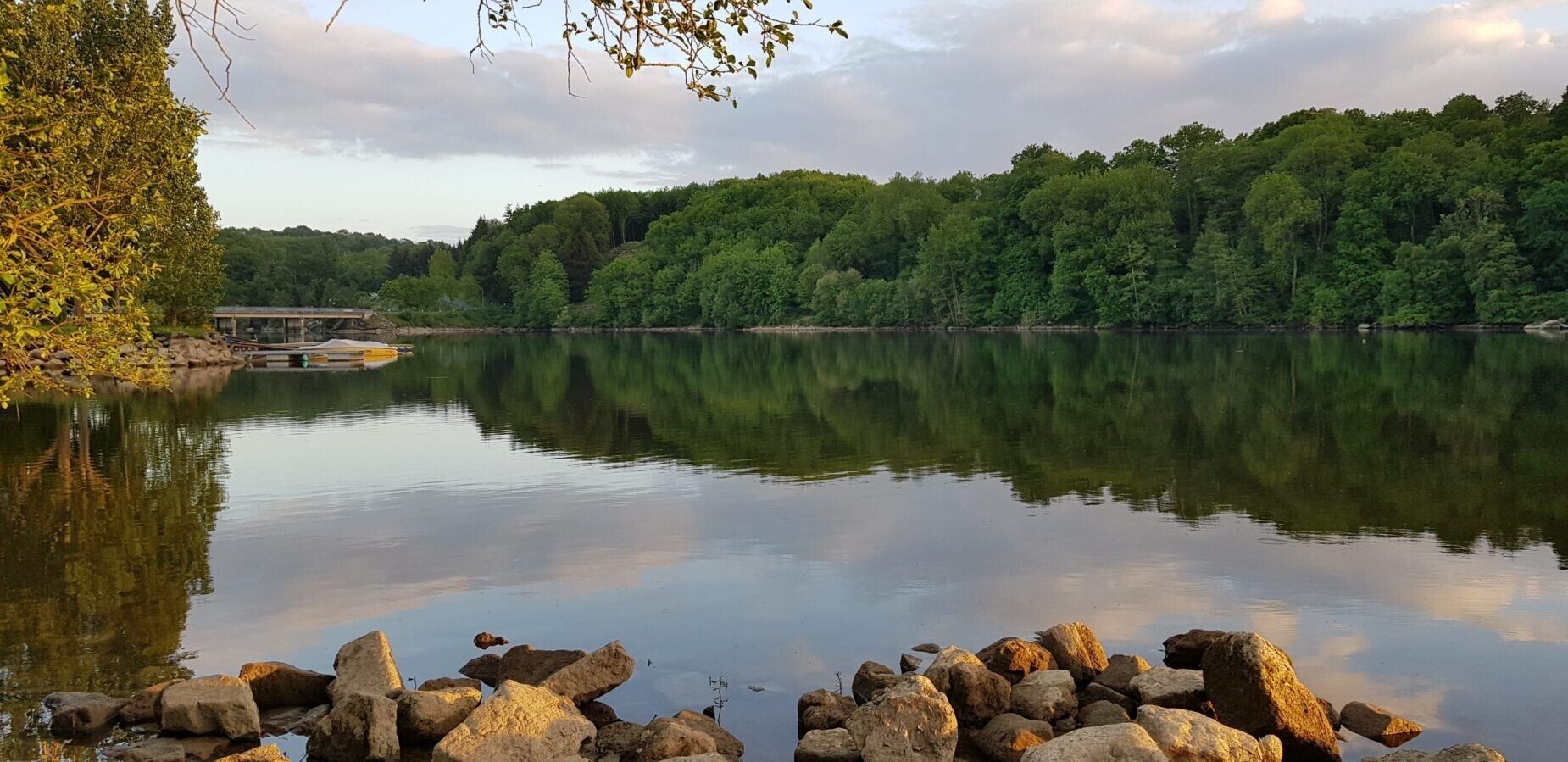 A calm lake with a rocky shoreline, dense forest in the background, and a small dock.