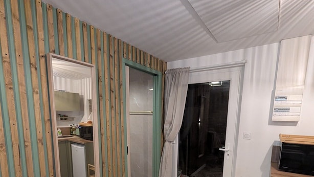 Ein Zimmer mit Fischgrätparkett, einem spiegel mit Holzrahmen, einer Schiebeglastür und einem kleinen, weißen Kühlschrank.