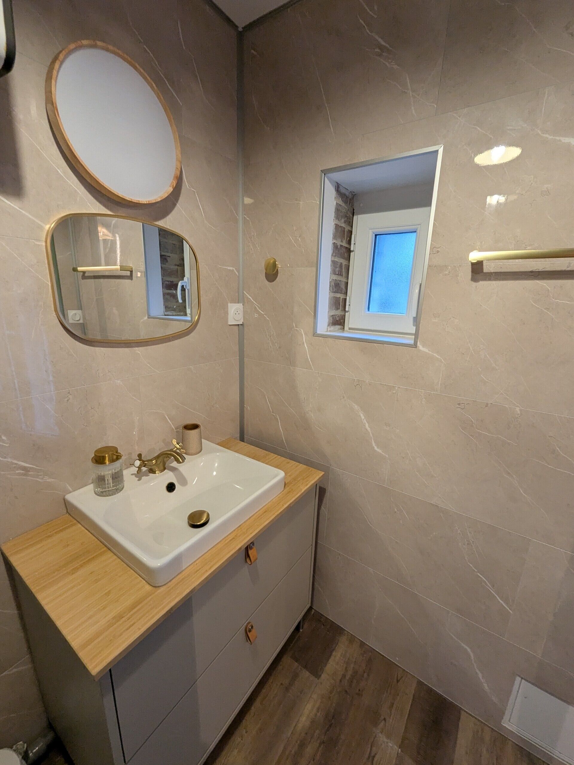 A bathroom with a wooden vanity, a white sink, a mirror, and a small window.