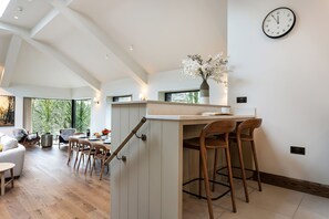A modern kitchen with a bar area, wooden chairs, and a clock on the wall. - The Old Bunkhouse (Ambleside)