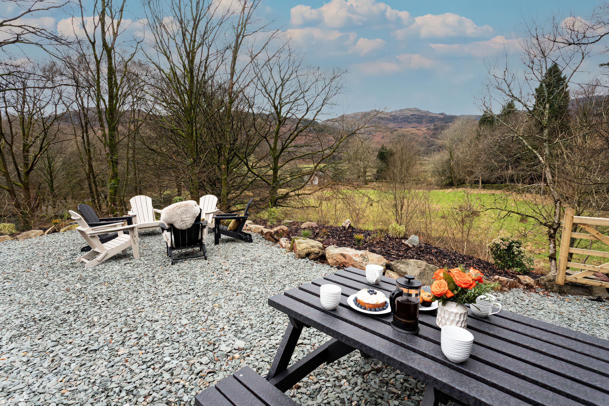 Un coin pique-nique aménagé avec une table, des chaises et une vue panoramique sur des collines et des arbres.