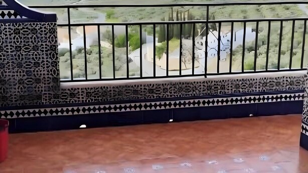 Ein Balkon mit Blick auf eine Landschaft, ein gemustertes Verlies und ein Tisch mit Stühlen.
