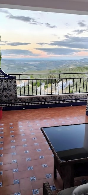 Un balcón con vistas a un paisaje, suelo estampado y una mesa con sillas.