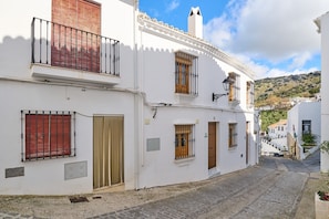 Una estrecha calle empedrada bordeada por edificios blancos con balcones, puertas de madera y ventanas con rejas.