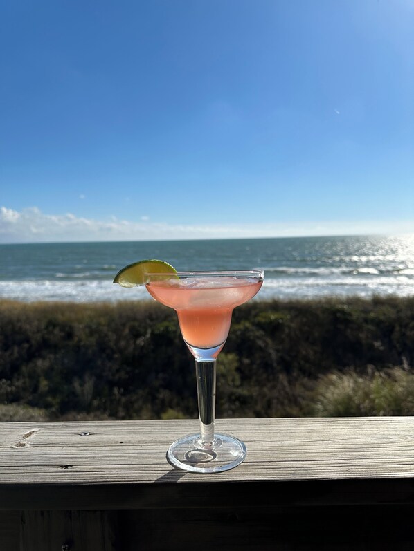 Een cocktailglas op een houten ondergrond, met uitzicht op de oceaan op de achtergrond.