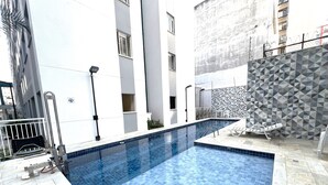 En swimmingpool med kakelbeklädd botten, ett staket av metall och en vägg med ett geometriskt mönster.