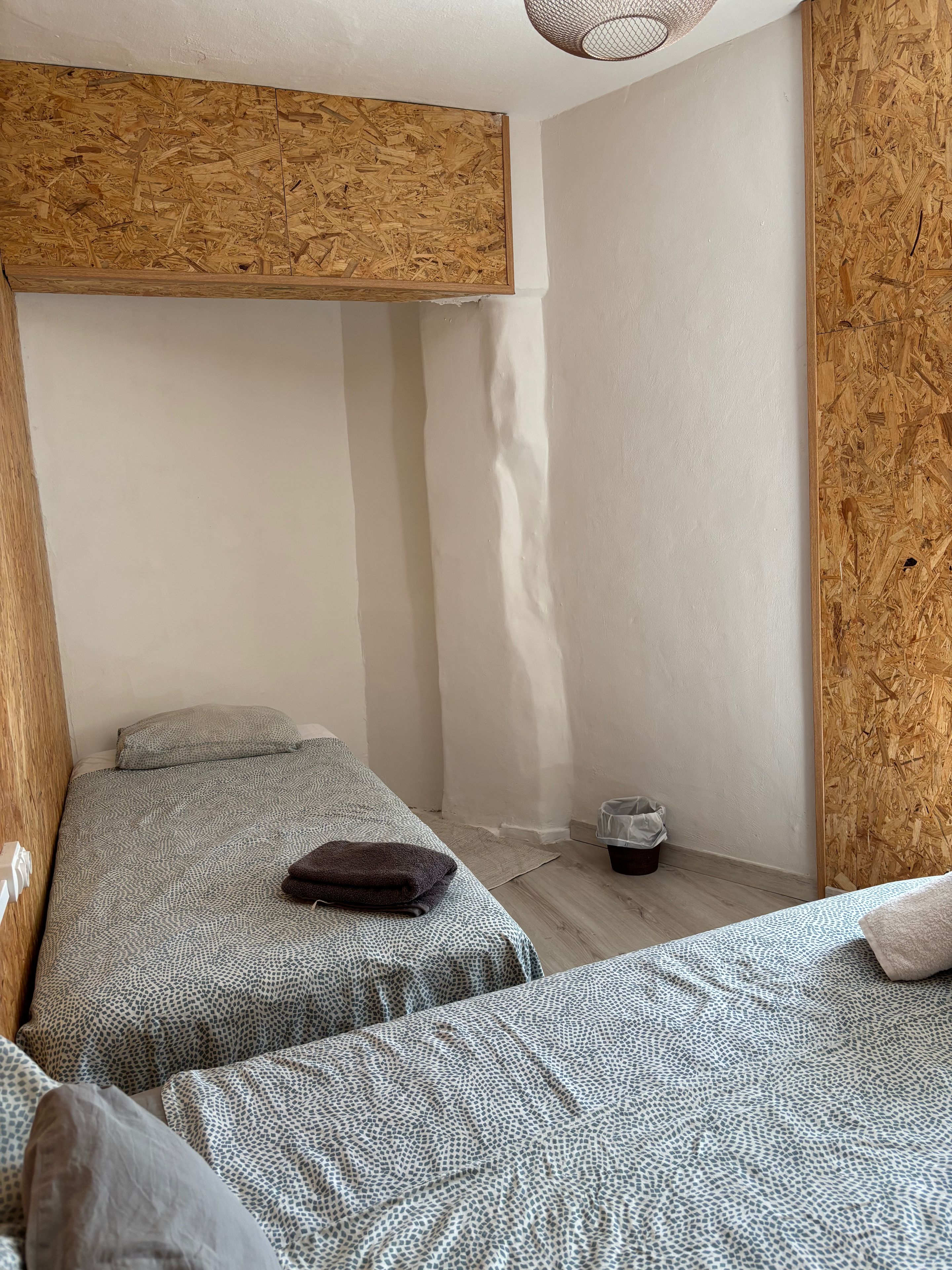 Een kamer met twee bedden, een houten plafond en een kleine prullenbak.