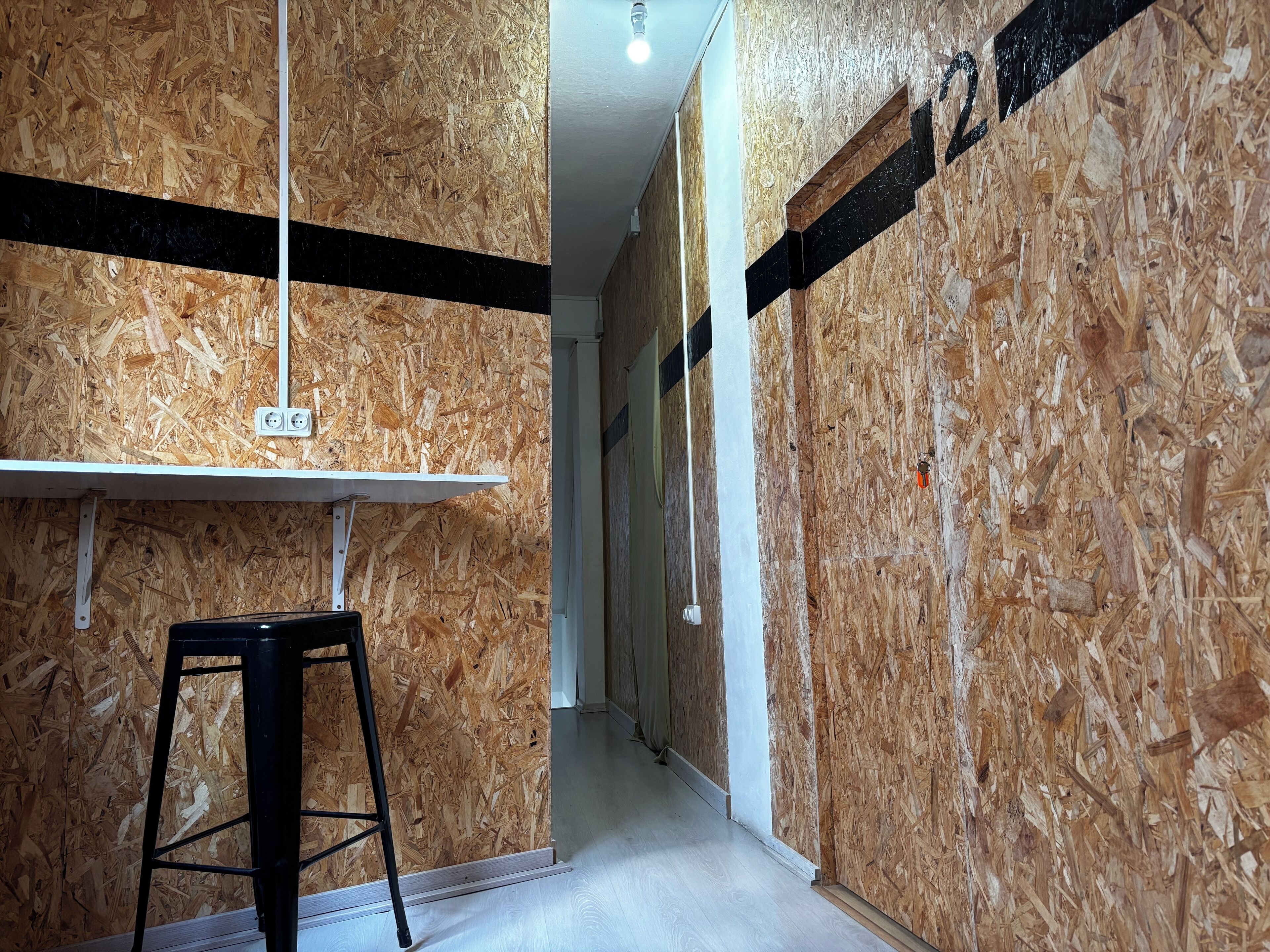 A narrow hallway with wooden paneling, a white ceiling, and a black metal stool.