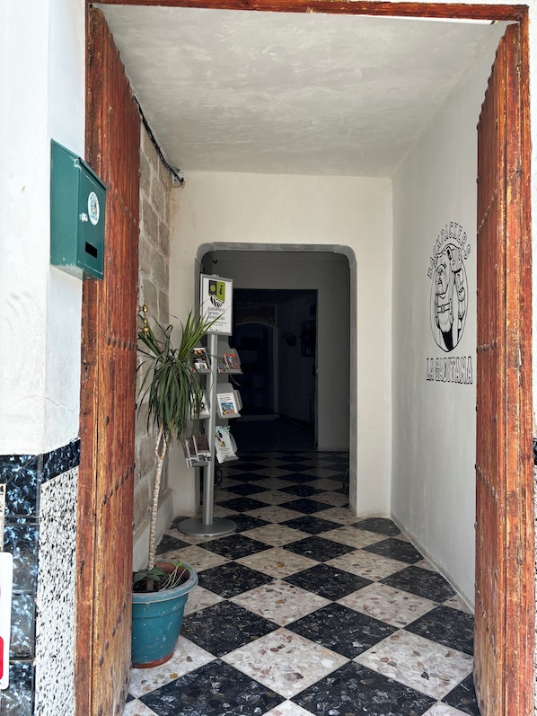 Un couloir avec un sol à carreaux, un cadre de porte en bois, une boîte aux lettres verte et une enseigne fixée au mur.