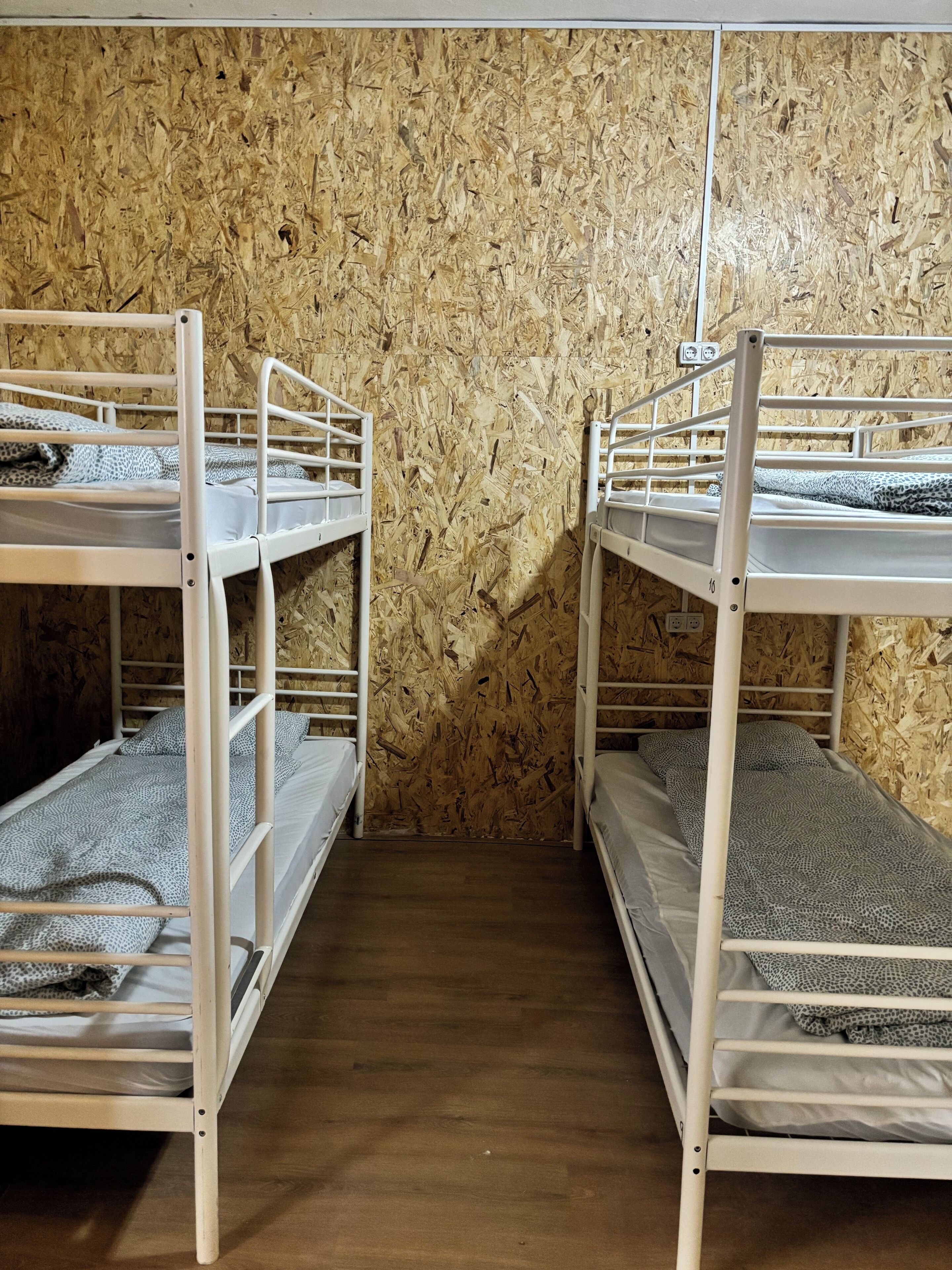 Een kamer met stapelbedden tegen een houten wand, een houten vloer en een stopcontact op de muur.