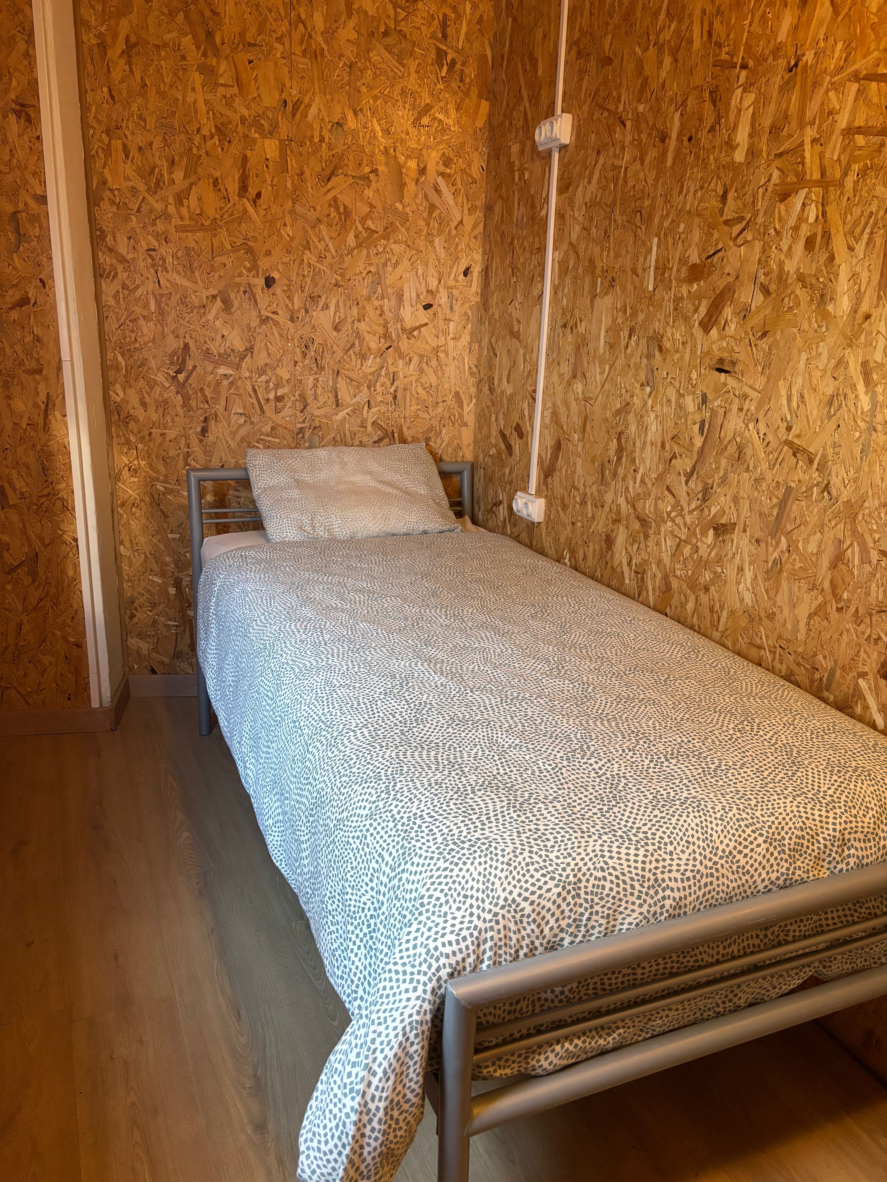 A single bed with a patterned bedspread in a room with wooden walls and a wooden floor.