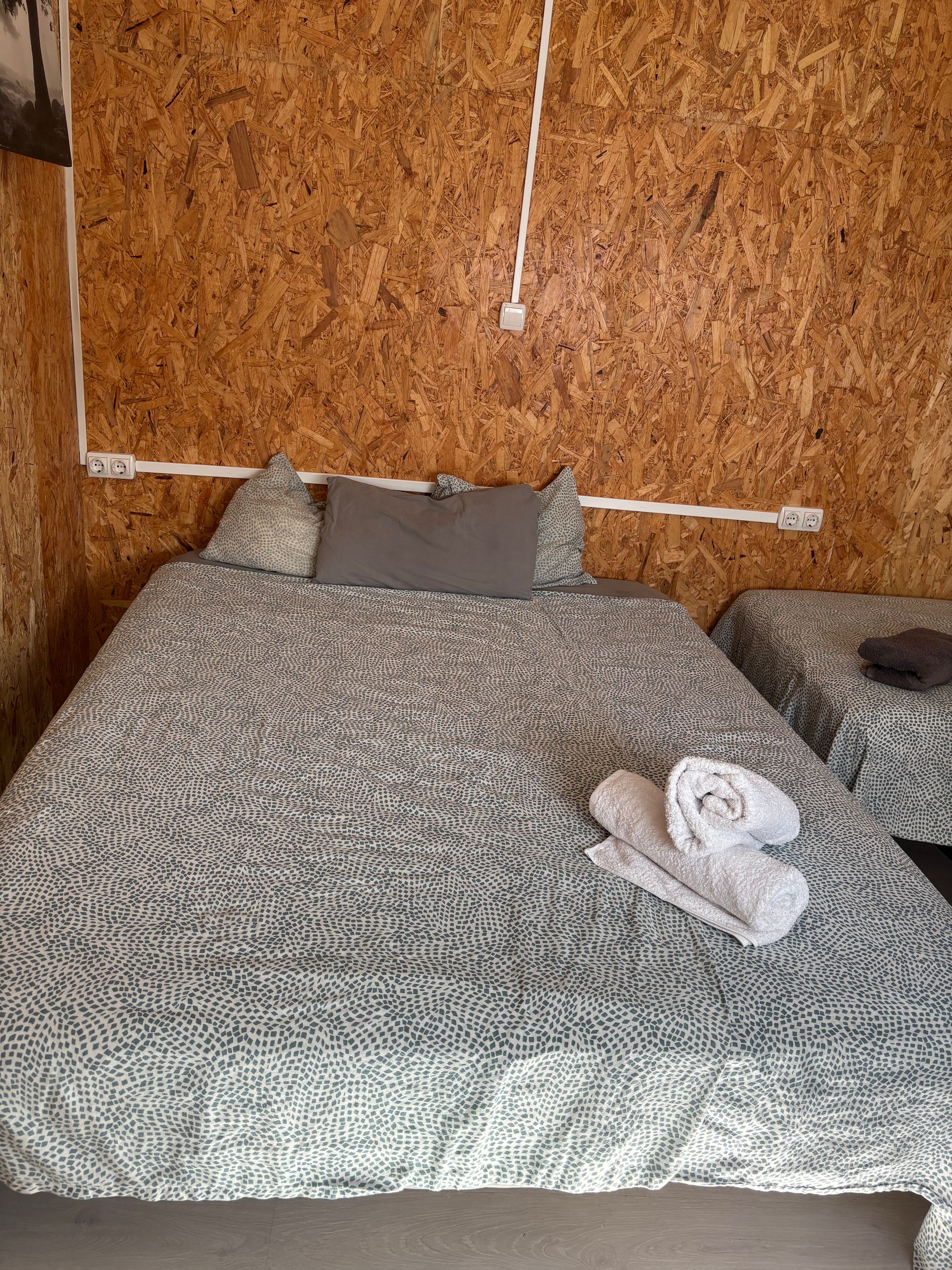 Una habitación con cama, mesita de noche y una pared cubierta de virutas de madera.