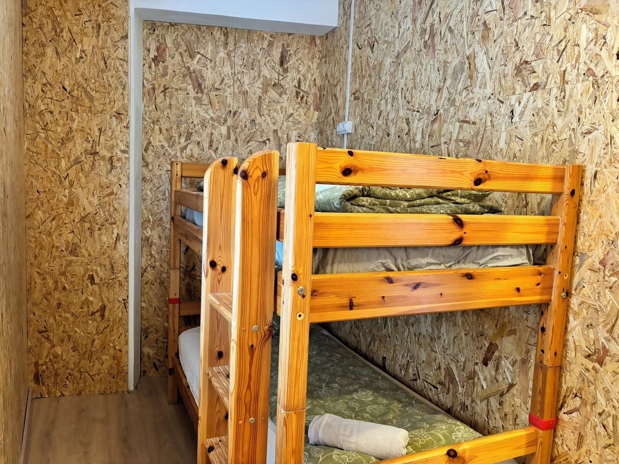 Una cama litera con estructura de madera y un colchón con funda verde.