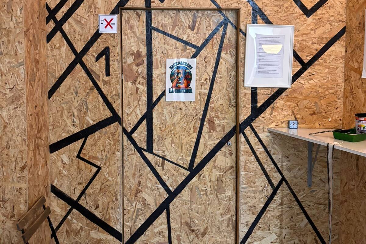 A room with a wooden wall, a door marked with a number, a poster, and a small table with a clock.