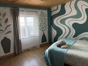 A bedroom with a bed, a window with sheer curtains, a wall with a leaf pattern, and a wavy design on the wall. - Backpackers La Gaditana (Alhaurín el Grande)