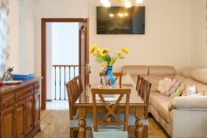 A dining area with a wooden table and chairs, a vase with flowers, and a sofa with cushions. - Casa Rural Martemma: Mountain Views, Private Pool, and Air Conditioning (Zuheros)