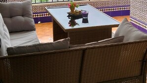 Un balcone con un divano in vimini, un tavolino con un vaso e vista su un paesaggio collinare.