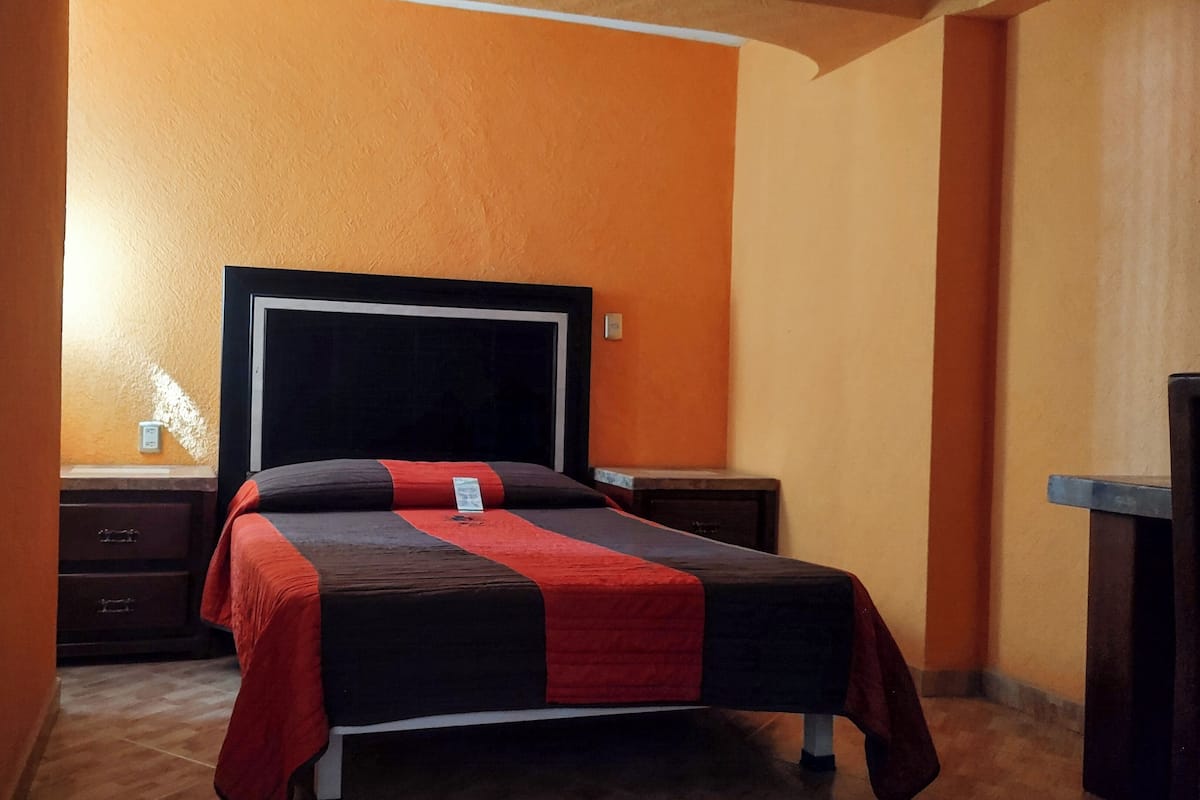 Een hotelkamer met een bed, nachtkastje, dressoir en bureau.