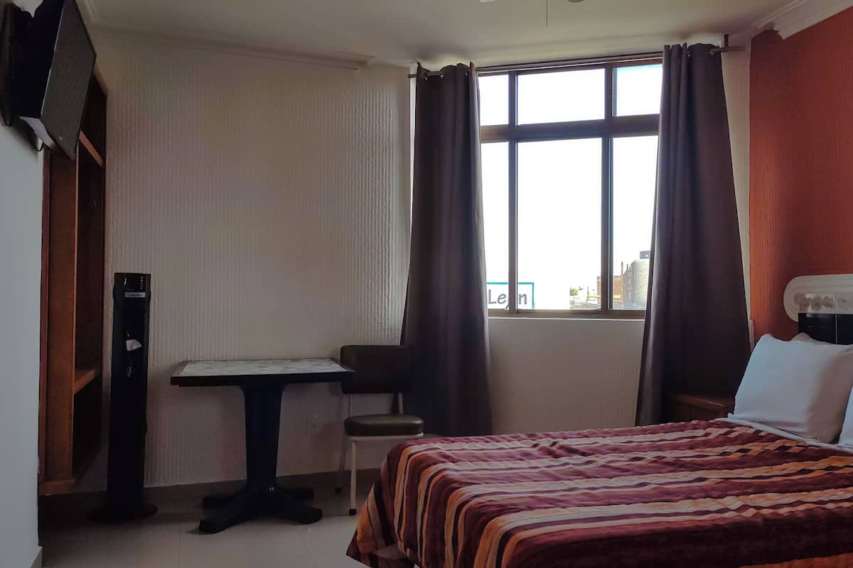 Een hotelkamer met een bed, een bureau en een raam met gordijnen.