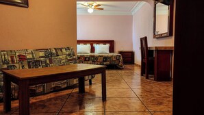 A hotel room with a wooden sofa, a bed with patterned bedding, a small table, and a ceiling fan. - Hotel El Baron (León)