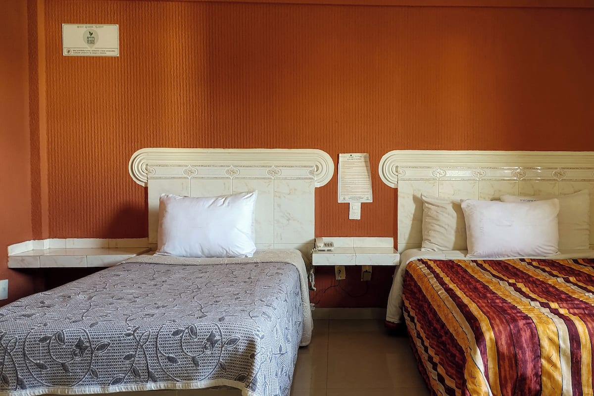 Een hotelkamer met twee bedden, elk met een witte hoofdbord en een nachtkastje. Tussen de bedden hangt een telefoon aan de muur.