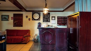 A cozy room with a red sofa, a wooden cabinet, a clock, and a wall with framed pictures and a menu. - Hotel El Baron (León)