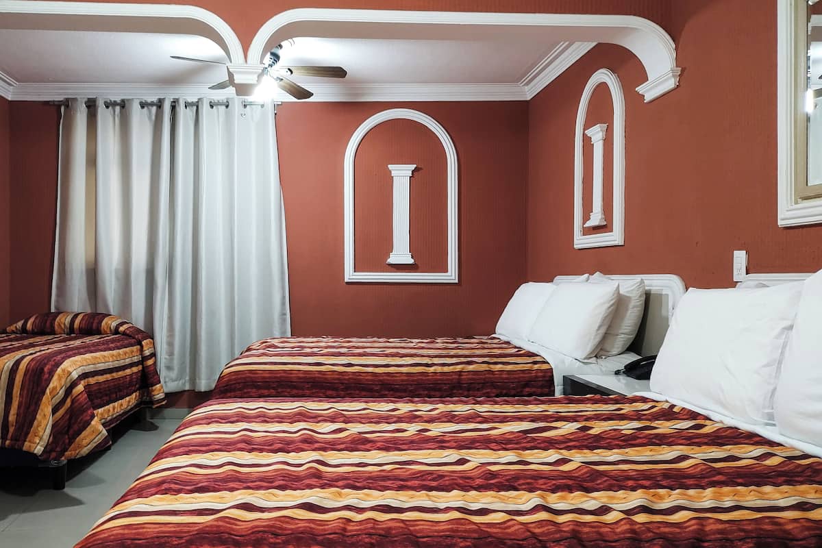 Een hotelkamer met twee bedden, een plafondventilator en een raam met gordijnen.