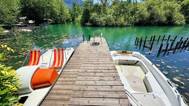 A wooden dock extending into a calm body of water, surrounded by lush greenery and trees.